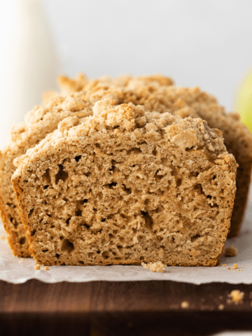 apple bread on a piece of parchment paper on a wooden cutting board.