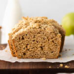 apple bread sliced on a white piece of parchment paper on a dark cutting board.
