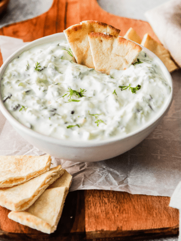 tzatziki sauce in a white bowl with a wooden spoon and pita on the side and dipped in the bowl