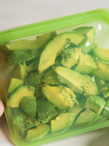 hand holding frozen avocado chunks in a reusable silicone stasher bag.