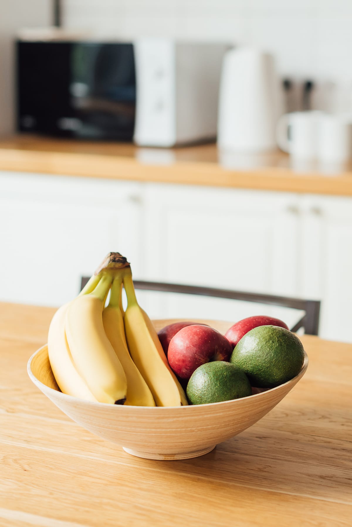 wooden basket with bananas, apples, and avocado on a countertop showing how to store avocado and other fruits to ripen the avocado.