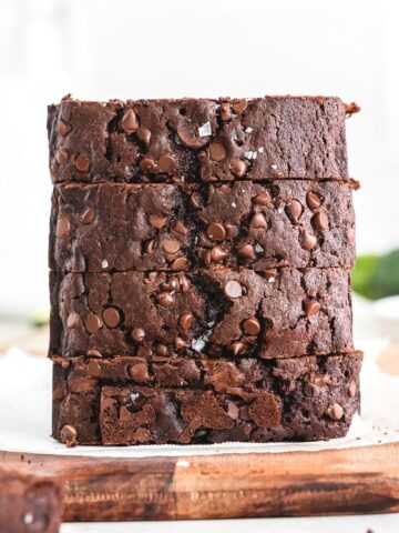 close up of sliced and stacked chocolate zucchini bread on a wooden cutting board with parchment paper on it.