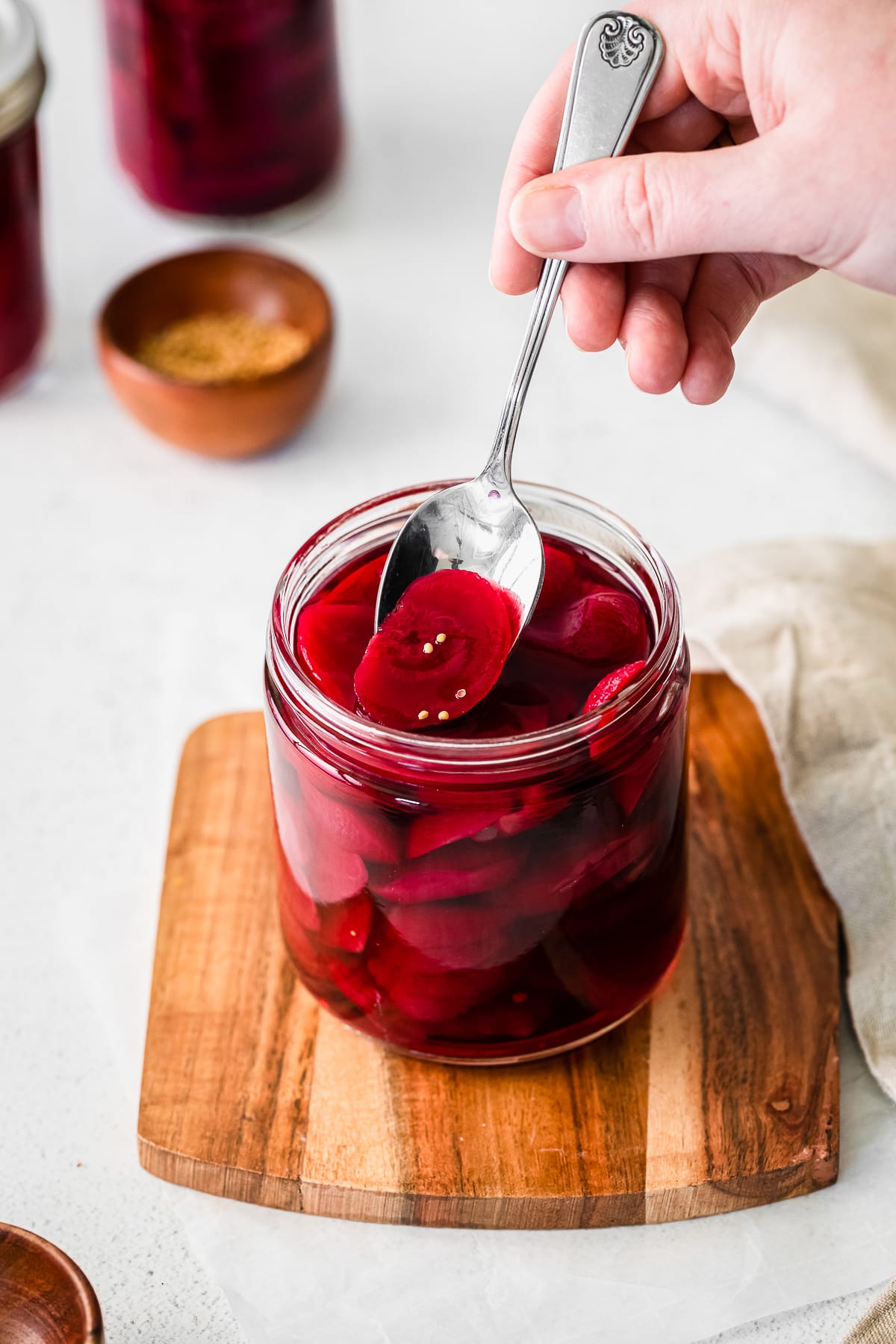 quick pickled beets in a glass jar on a cutting board with a hand holding a spoon taking some out.