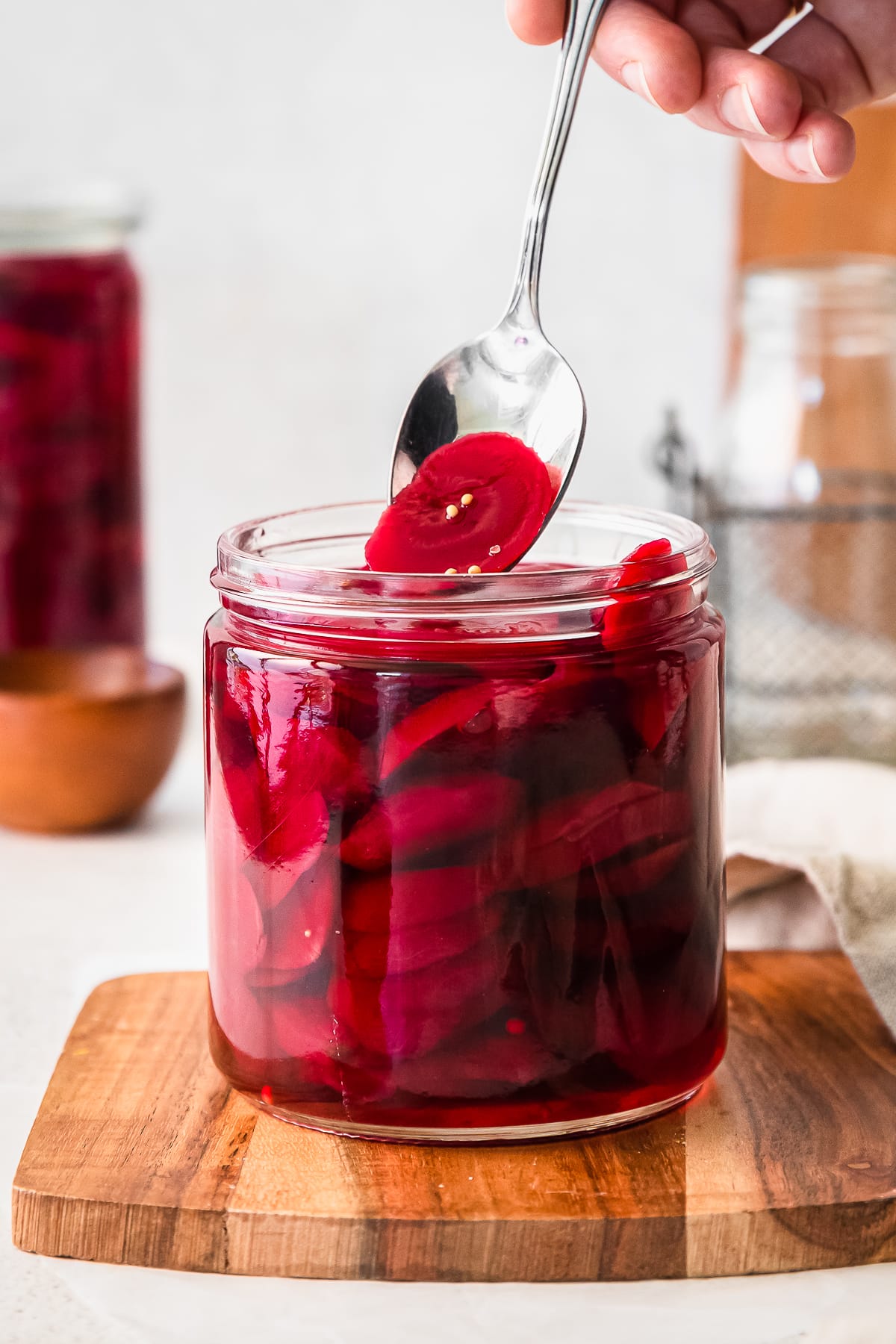 quick pickled beets in a glass jar on a cutting board with a spoon scooping a beet slice out.