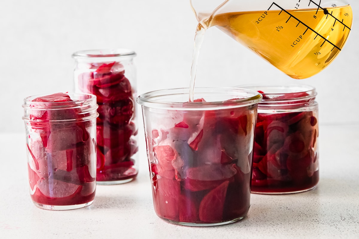 pickling mixture being poured into glass jars filled with beets.