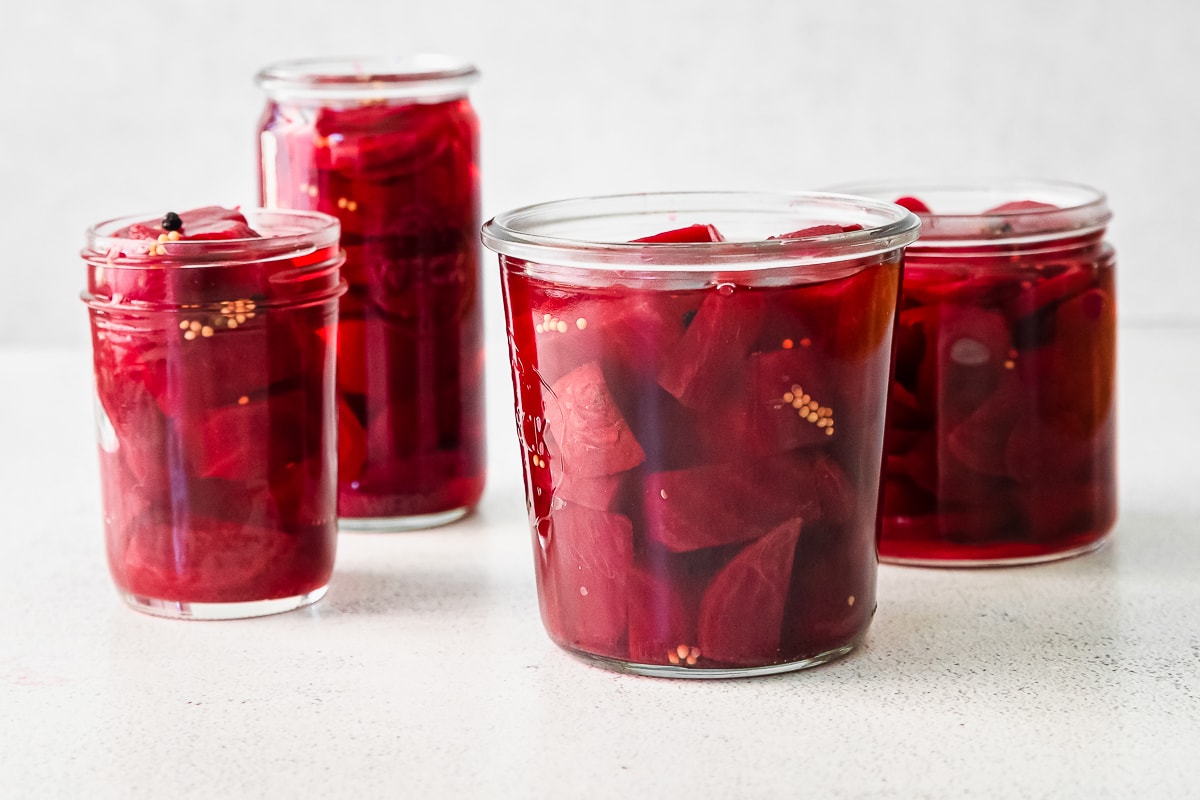 various glass jars filled with chopped and sliced beets and quick pickling mixture to make pickled beets.