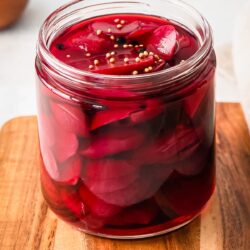close up of quick pickled beets in a glass jar on a cutting board.