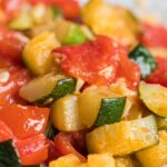 zucchini and tomatoes perfectly cooked in a white bowl.