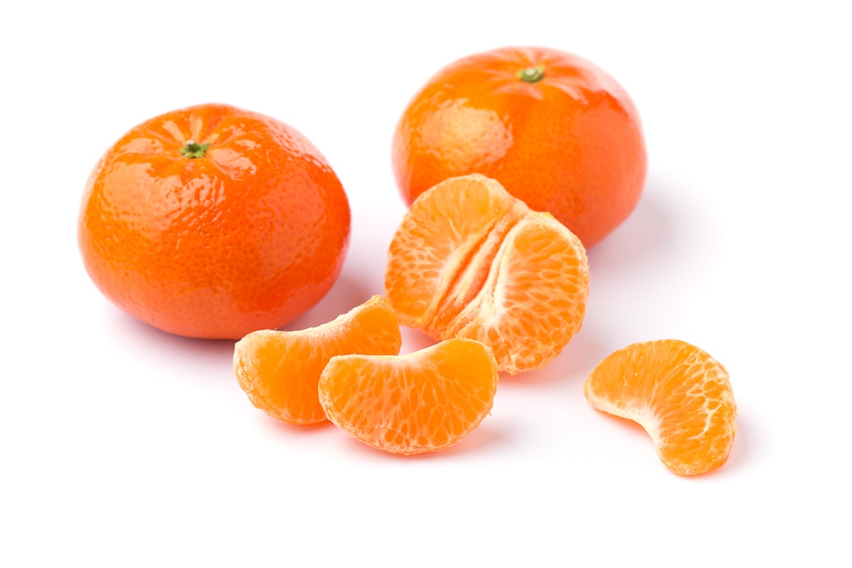 two whole clementines and one clementine peeled with segments laying on a white background.