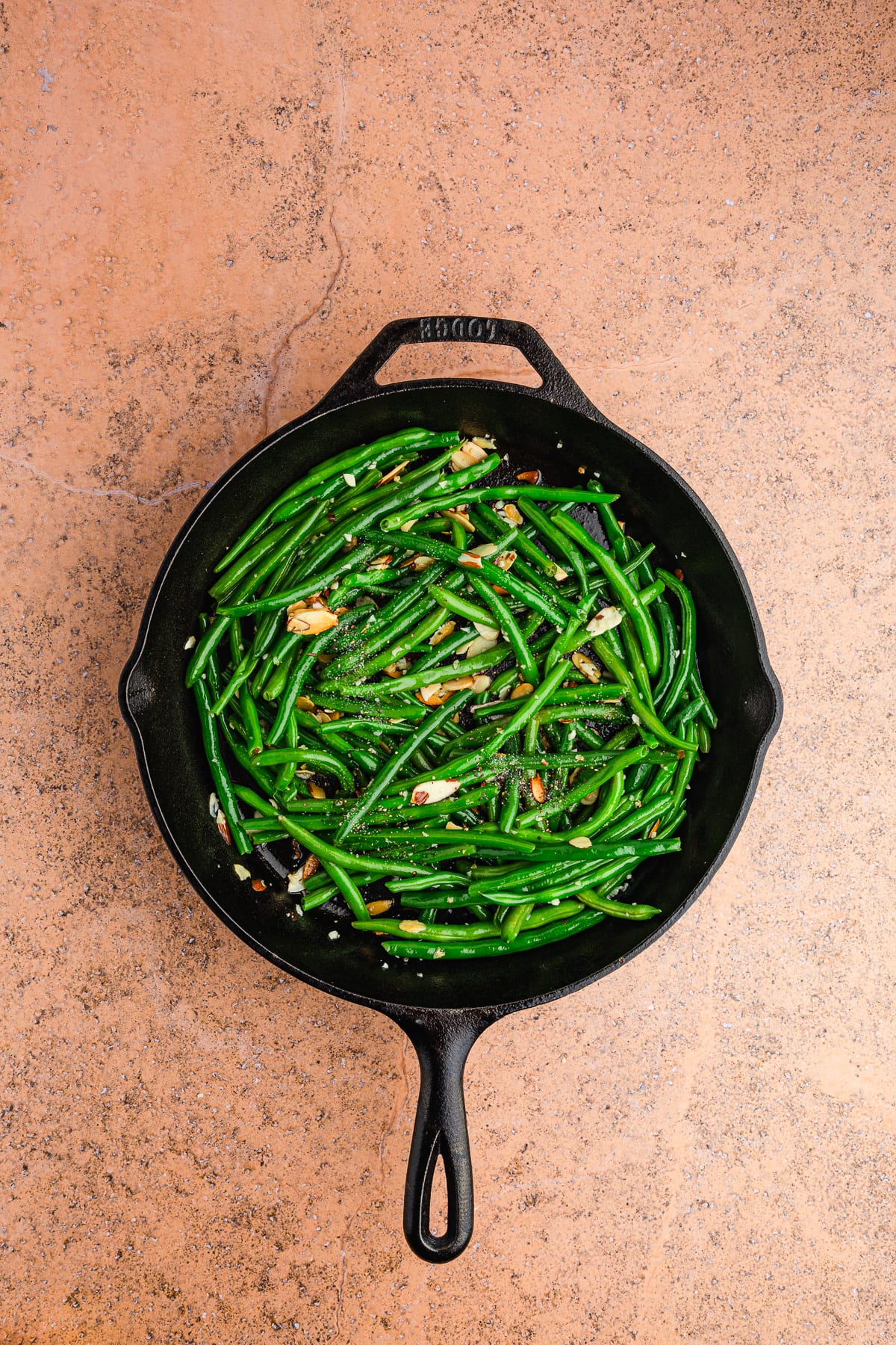 cooked green beans almondine in a cast iron pan with a wooden spatula.