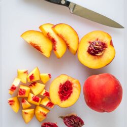 how to cut a peach step by step tutorial picture showing a paring knife, a whilte peach, a halved peach, sliced peaches, and peach chunks on a cutting board.