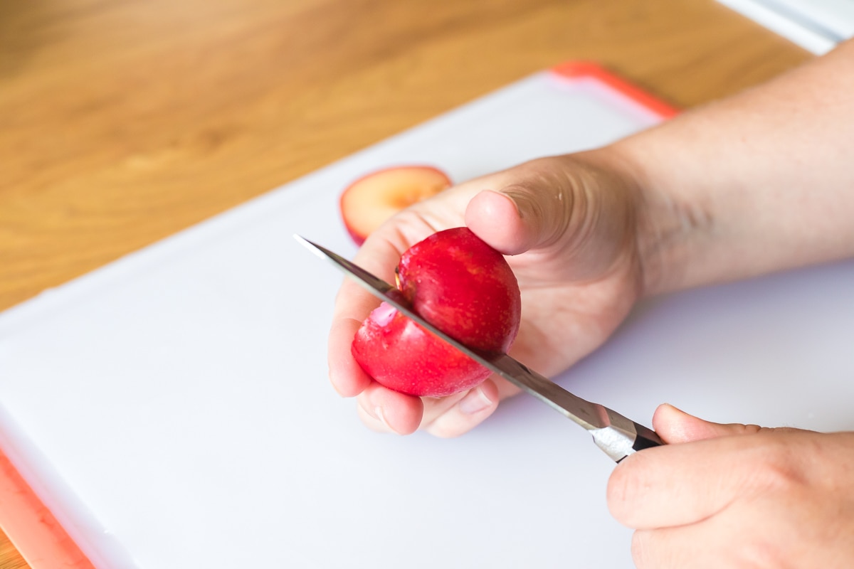 hand holding a paring knife cutting a plum in half.