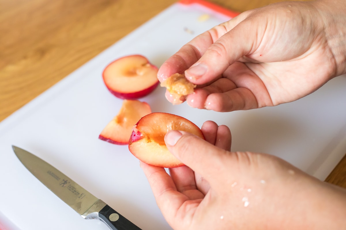 showing how to remove a plum pit hand holding a piece of plum and a plum pit in the other hand.