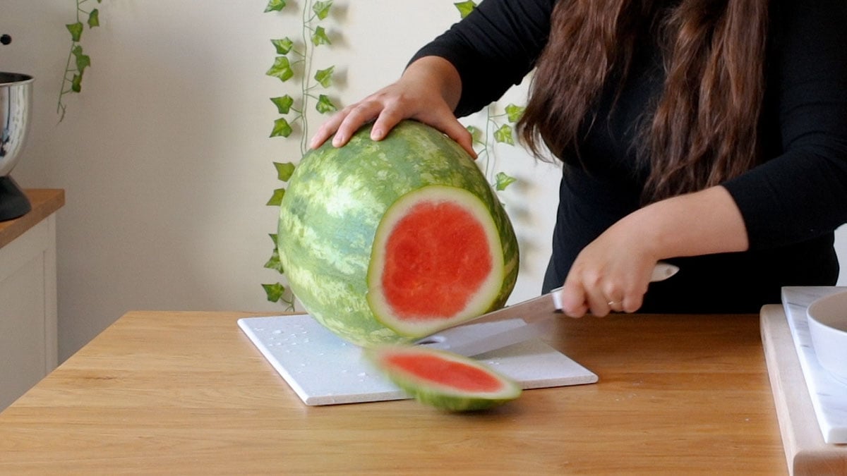 woman cutting a watermelon on a cutting board.
