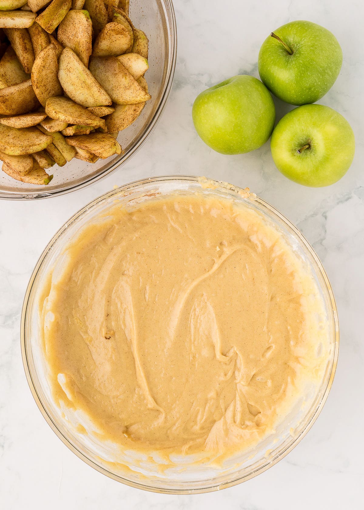 cake batter in a bowl with sliced apples and cinnamon sugar above.