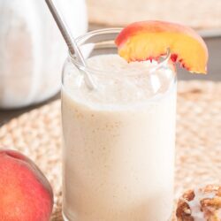 peach milk in a glass with a peach slice and straw.