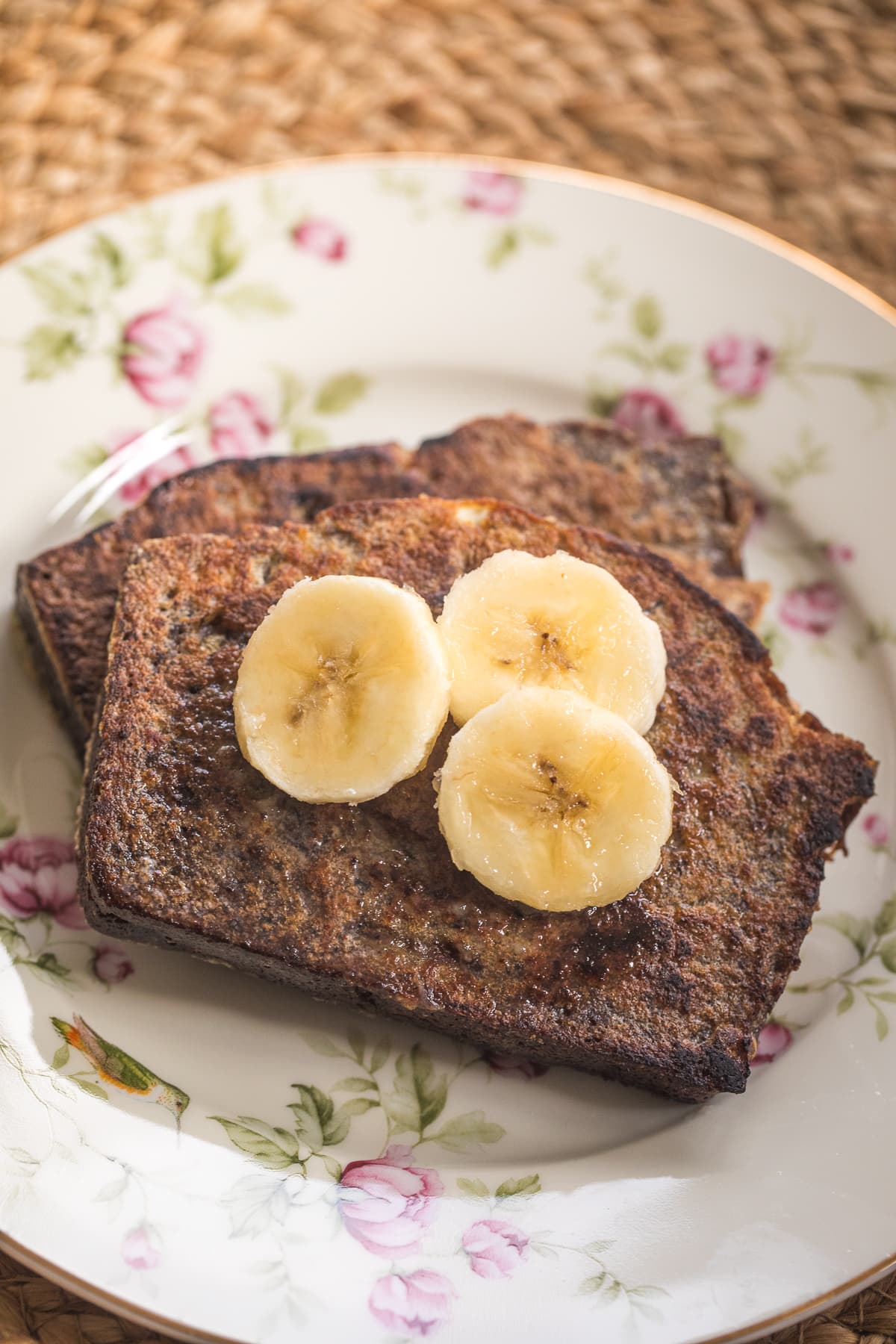 homemade banana bread french toast topped with banana slices on a plate.