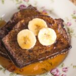 banana bread french toast on a plate with 3 banana slices and syrup.