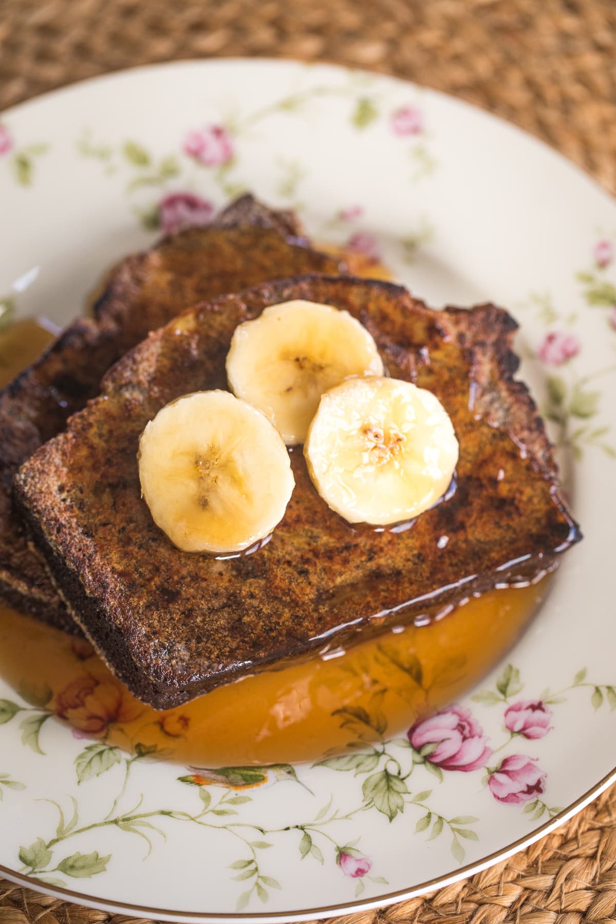 banana bread french toast on a plate with 3 banana slices and syrup.