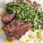 chimichurri steak close up photo over white rice on a white plate.