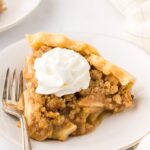 dutch apple pie on a white plate with a bit of whipped cream piped on it.