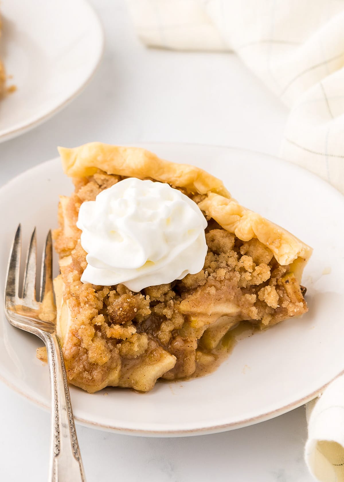 dutch apple pie on a white plate with a bit of whipped cream piped on it.