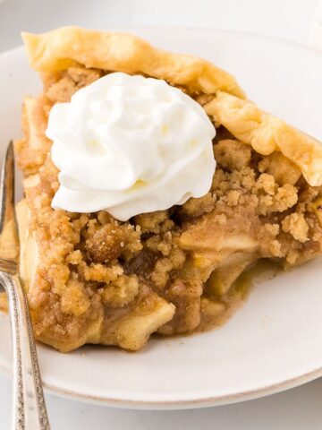 dutch apple pie slice on a plate with whip cream and a fork.