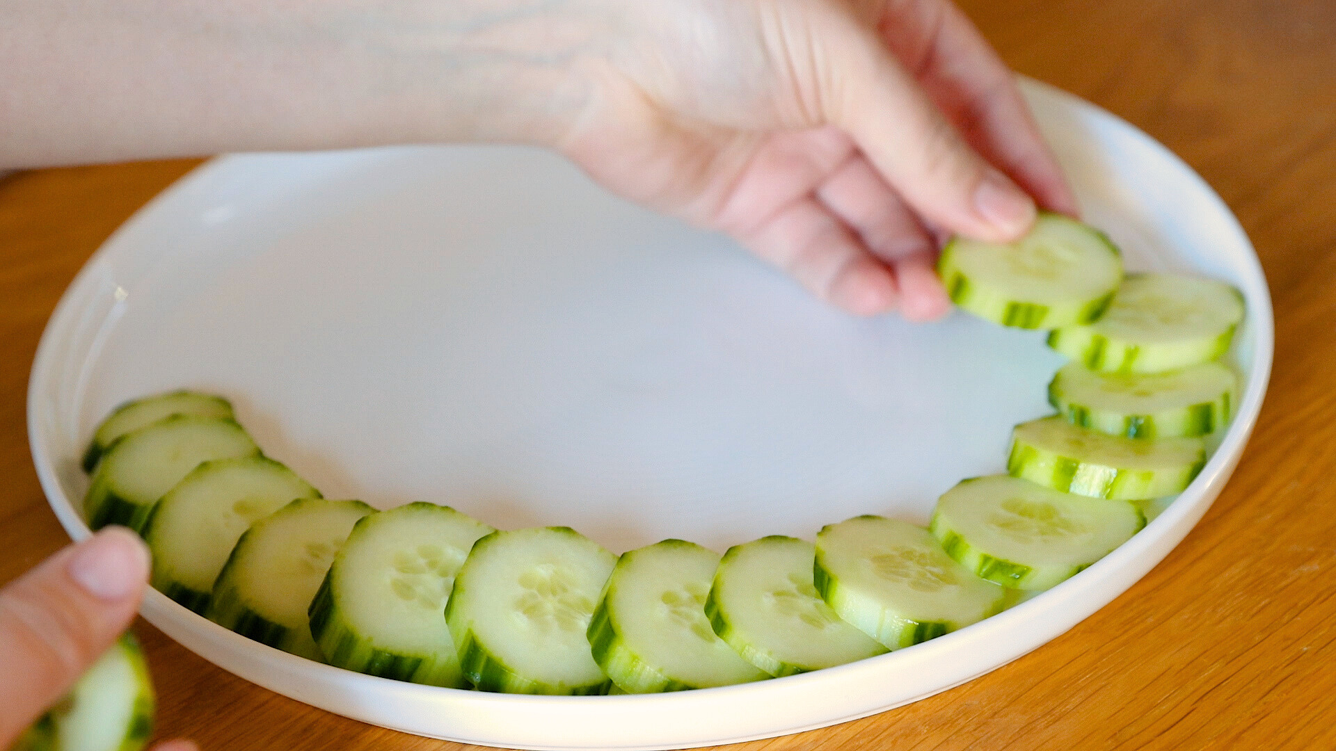 hands arranging sliced cucumbers on a veggie platter.