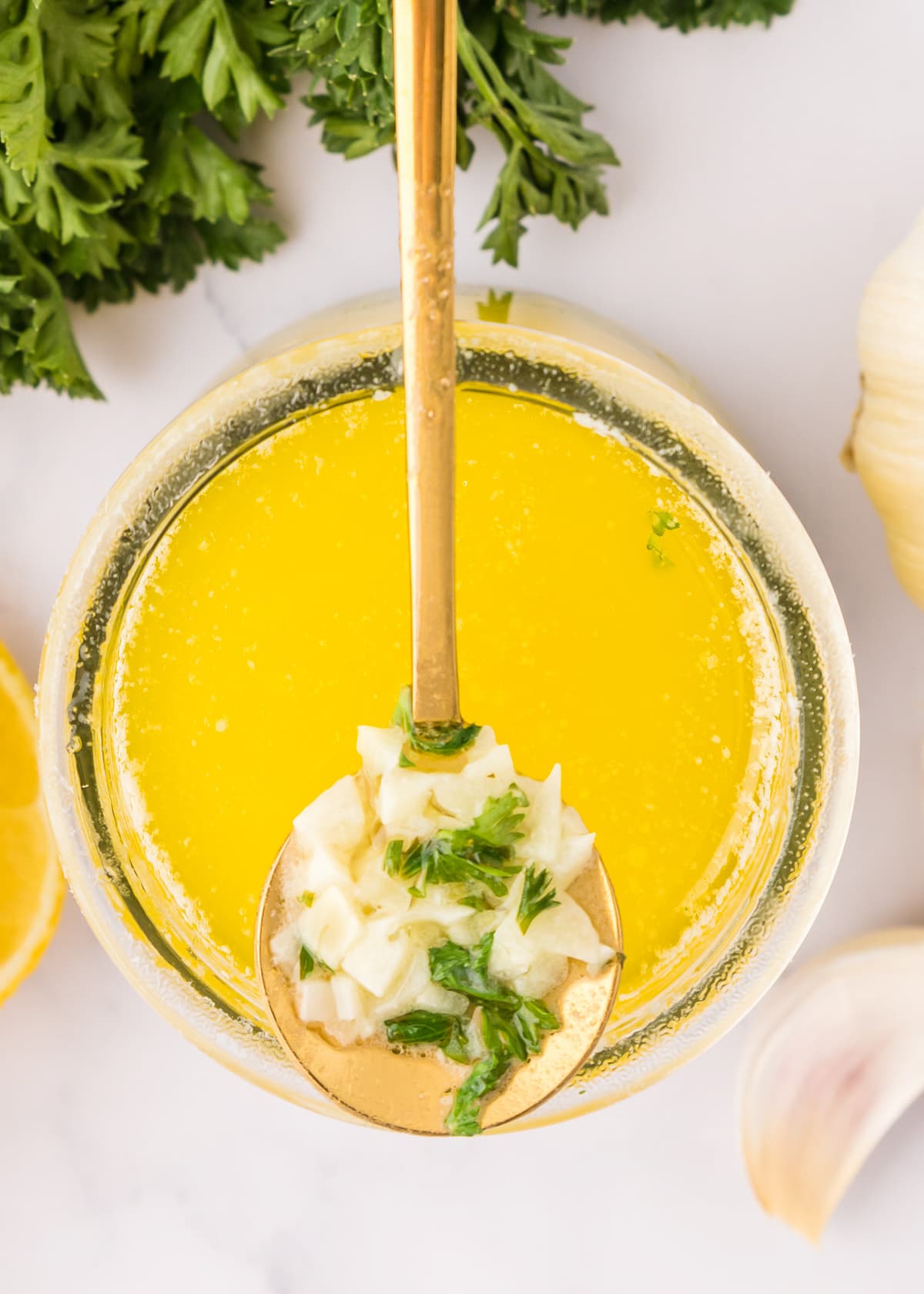 overhead photo of lemon garlic butter sauce in a glass jar with a spoon showing a scoop of the garlic. with fresh parsley cooked.