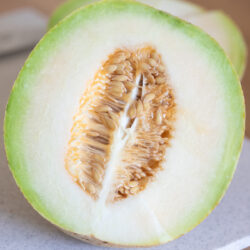 Summer Kiss melon cut in half on a cutting board showing the inside with the seeds still intact.
