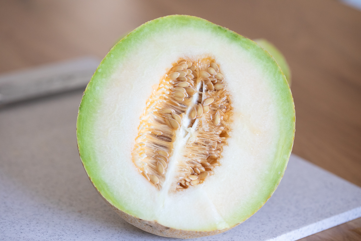 close up of Summer Kiss melon cut in half on a cutting board showing the inside with the seeds still intact.