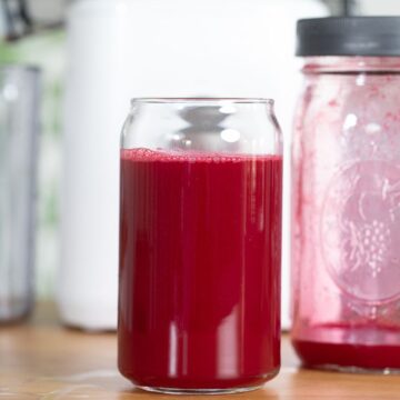 beet juice in a glass with an almost empty mason jar behind it.