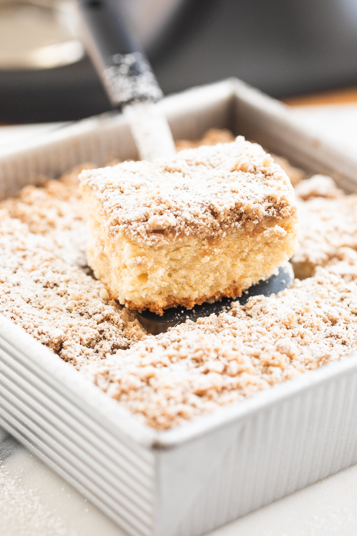 spatula holding a piece of crumb cake over a sheet pan of crumb cake slices.