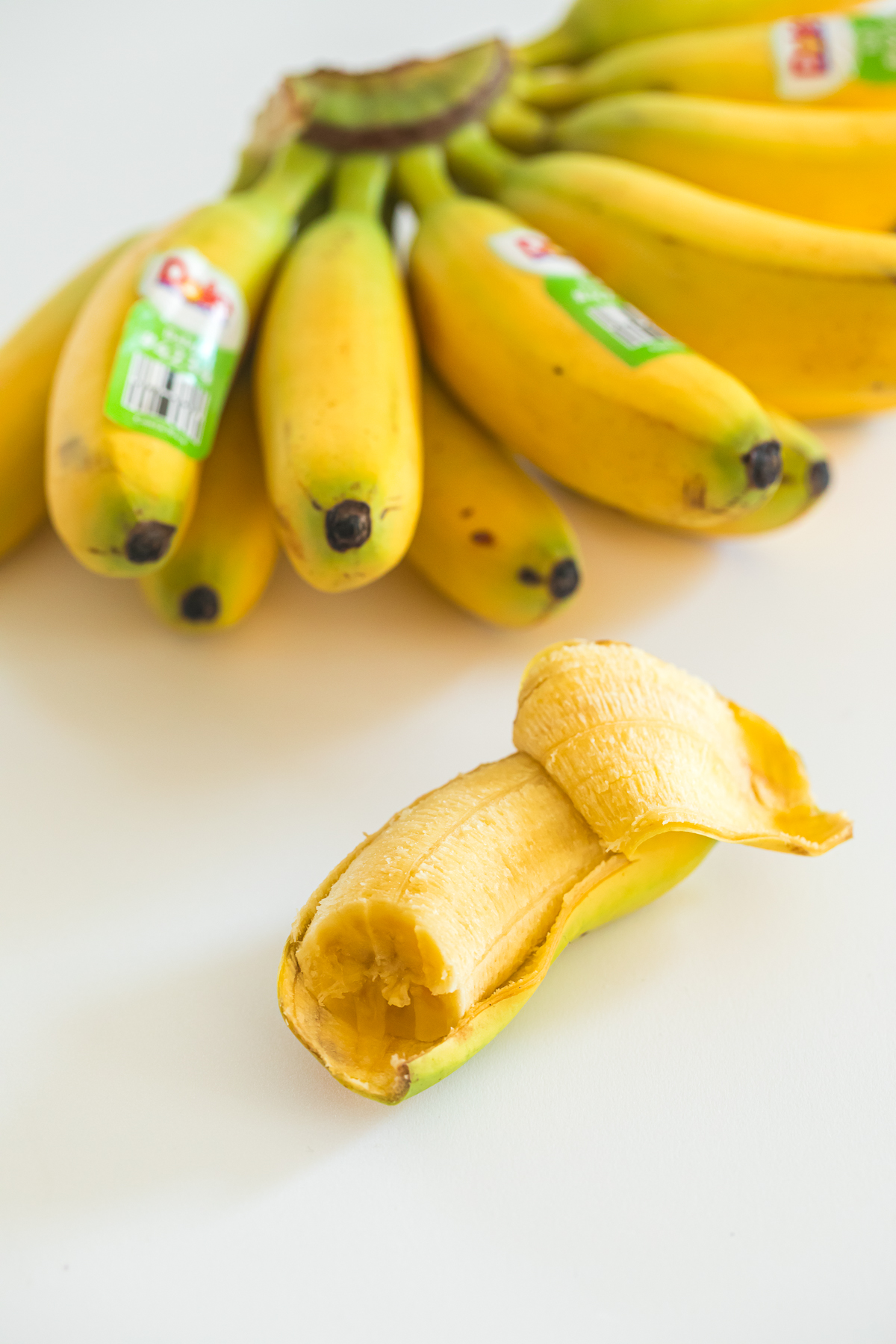 partially peeled baby banana with bite taken out and a bunch of baby bananas above it.