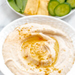 white bean hummus in a white bowl with a swirl and olive oil drizzle.