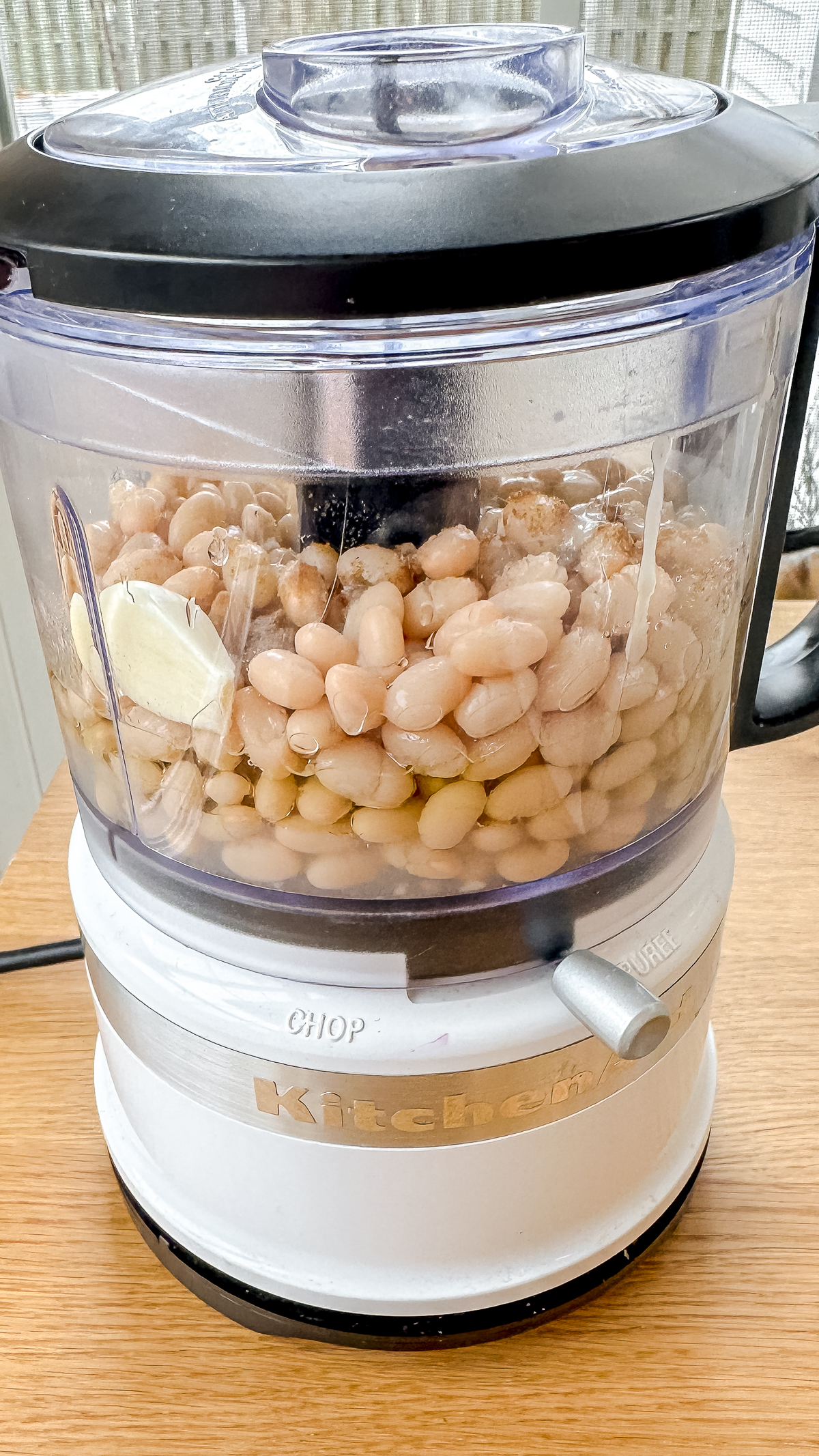 white beans, garlic, tahini, cumin, extra virgin olive oil, salt, and lemon juice in a food processor ready to process to make white bean hummus.