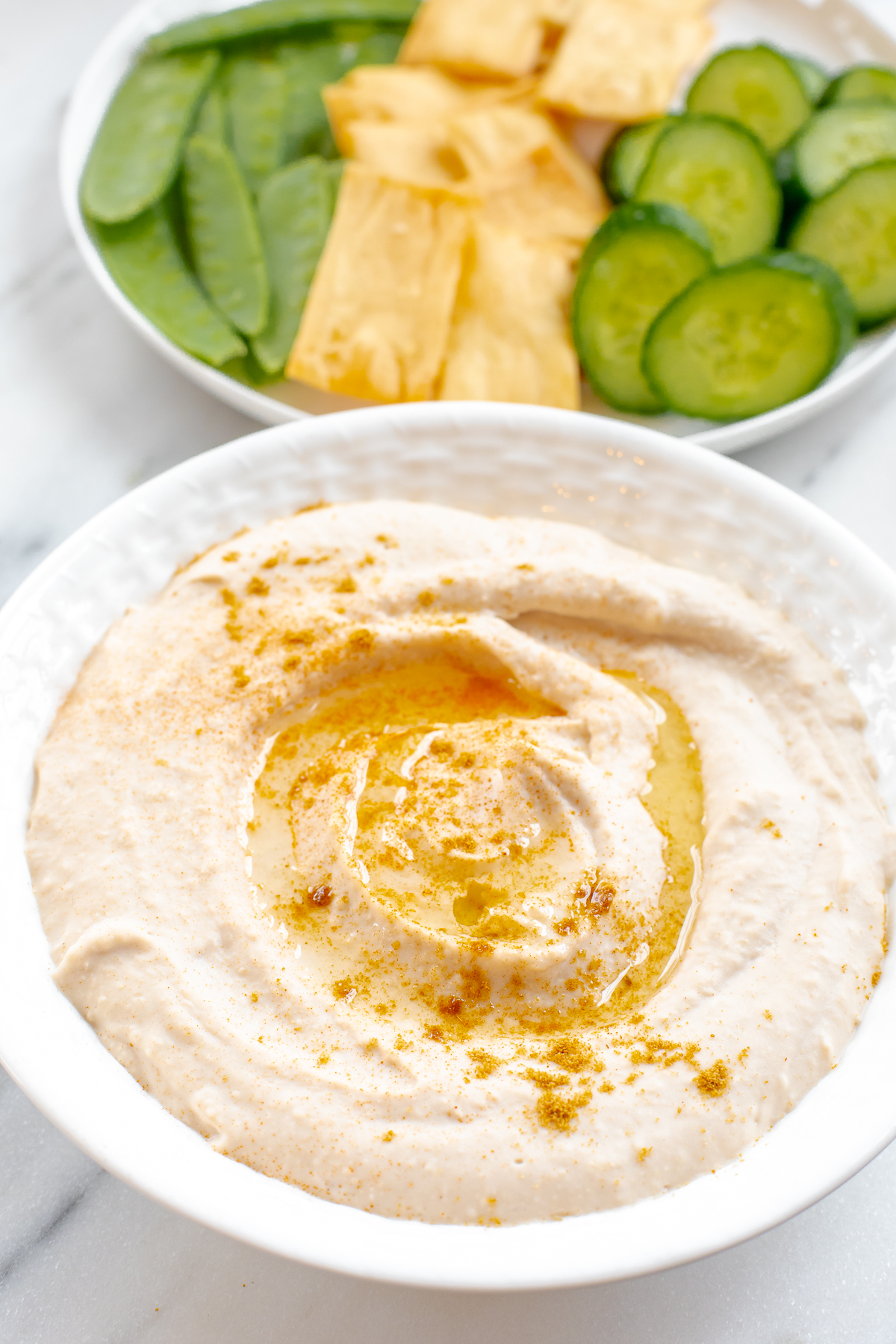 white bean hummus in a white bowl with a swirl and olive oil drizzle.