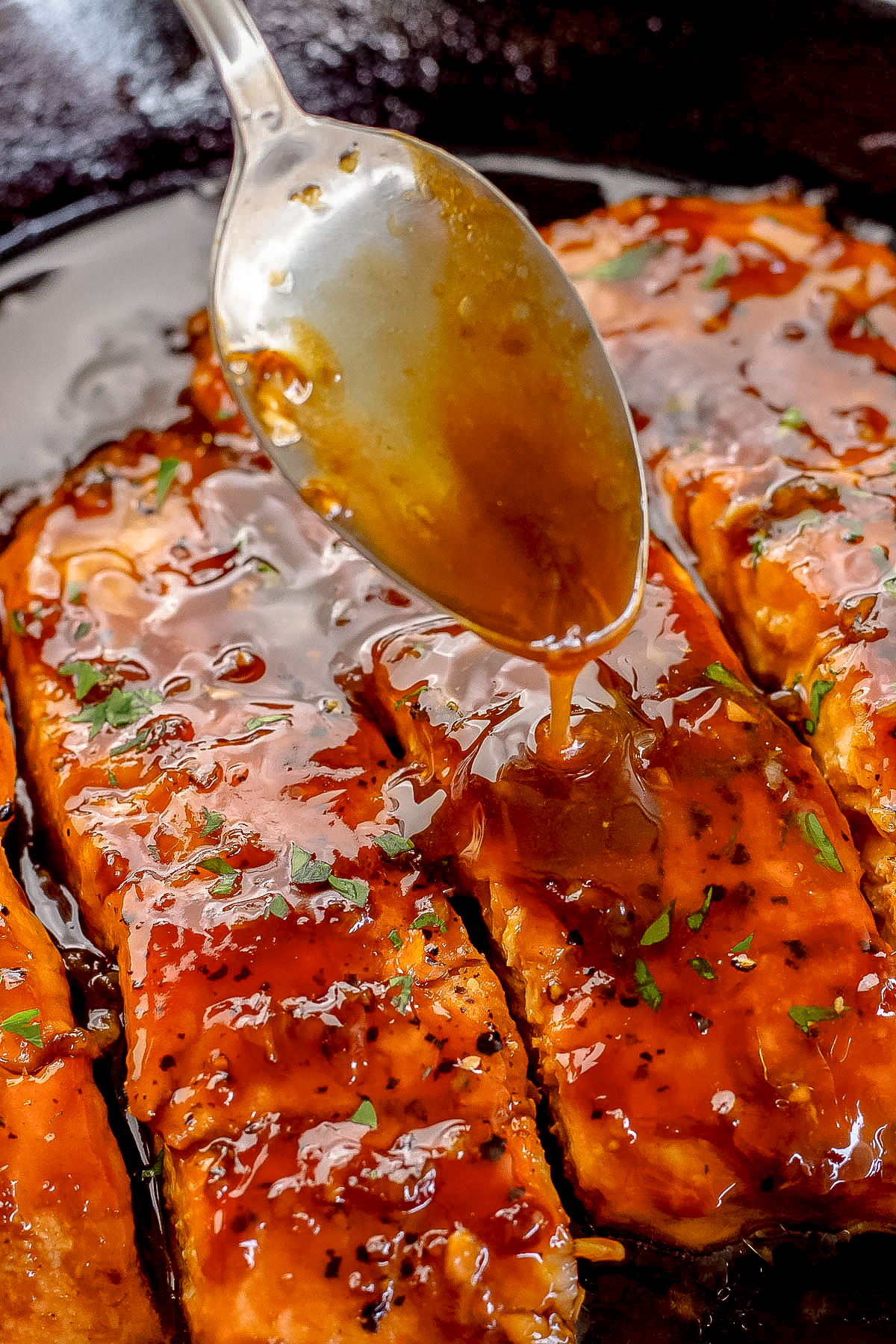 spoon drizzling honey garlic sauce over salmon in a cast iron skillet.