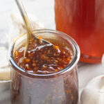 a small glass jar with honey garlic sauce with a spoon in it.