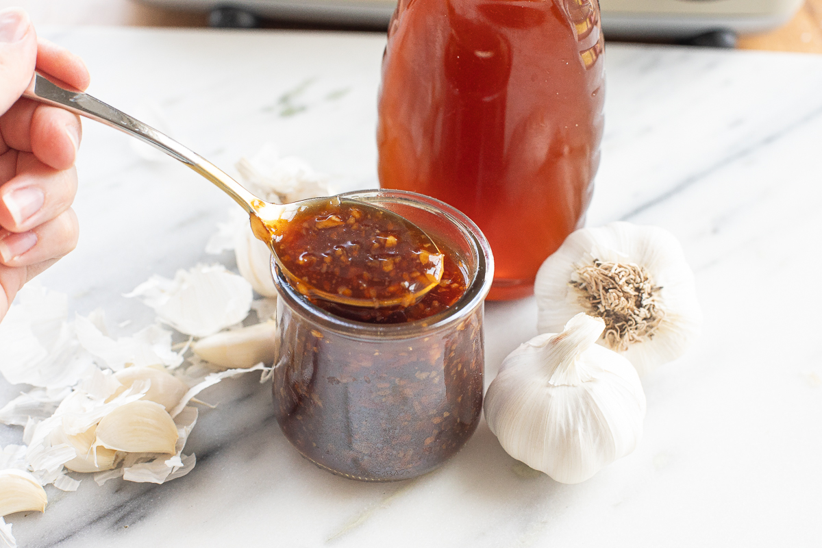 honey garlic sauce on a spoon above a glass jar with it inside.