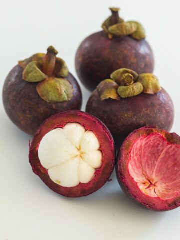 4 mangosteen with one being open to show white segments inside.