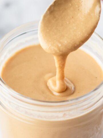 homemade tahini in a glass jar with spoon drizzling into it.