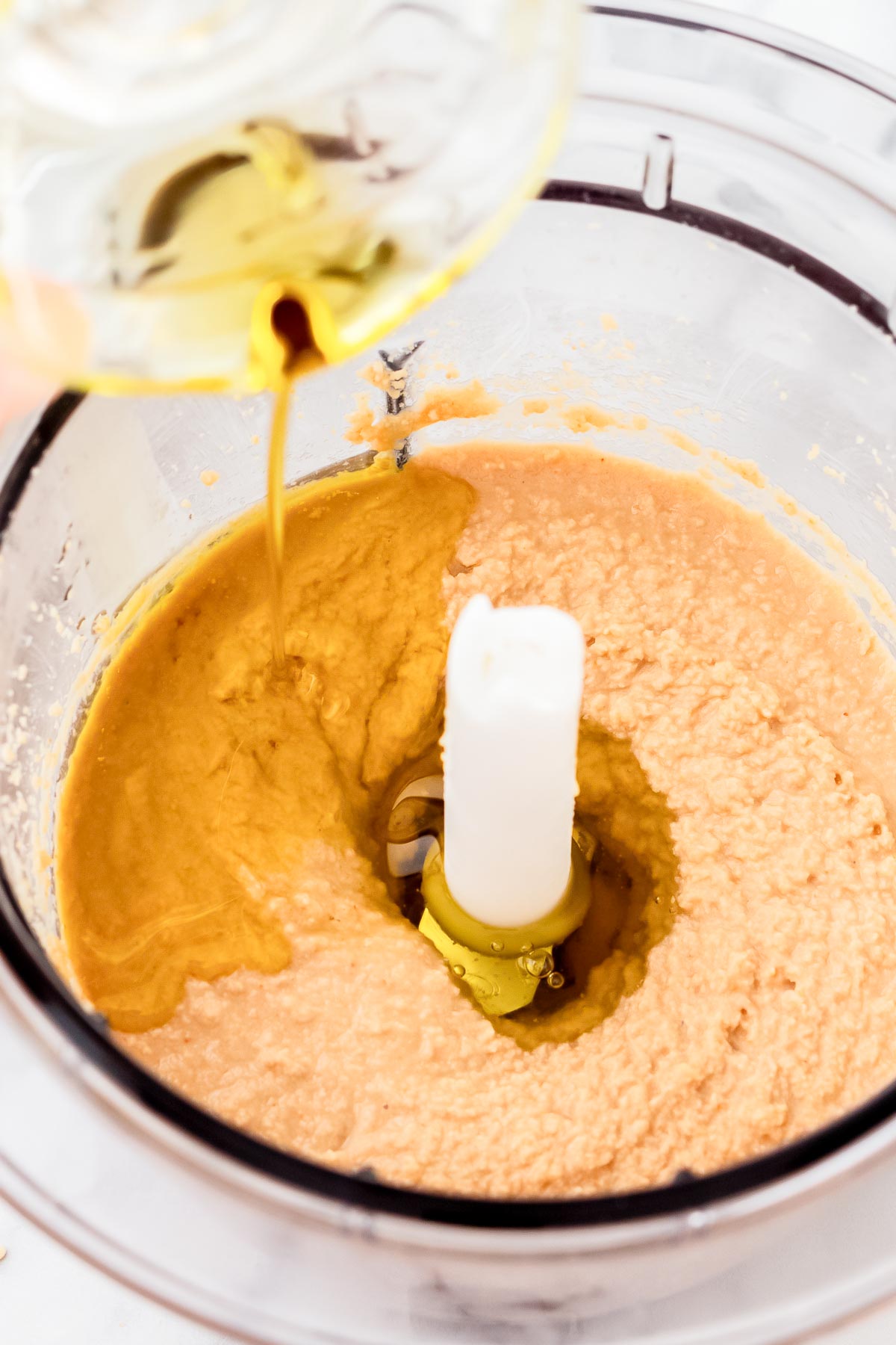 oil pouring into food processor with ground sesame seeds to make tahini.
