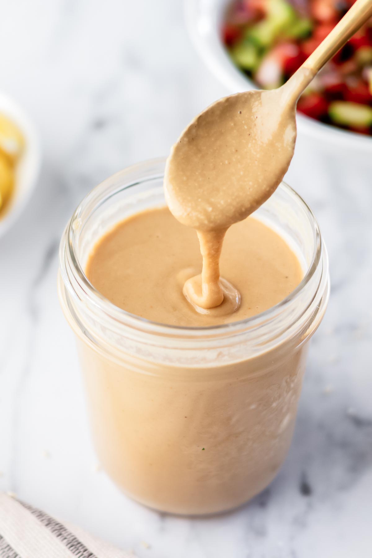 tahini drizzling into a glass jar with a spoon.