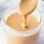 homemade tahini in a mason jar with a spoon drizzling it back in.
