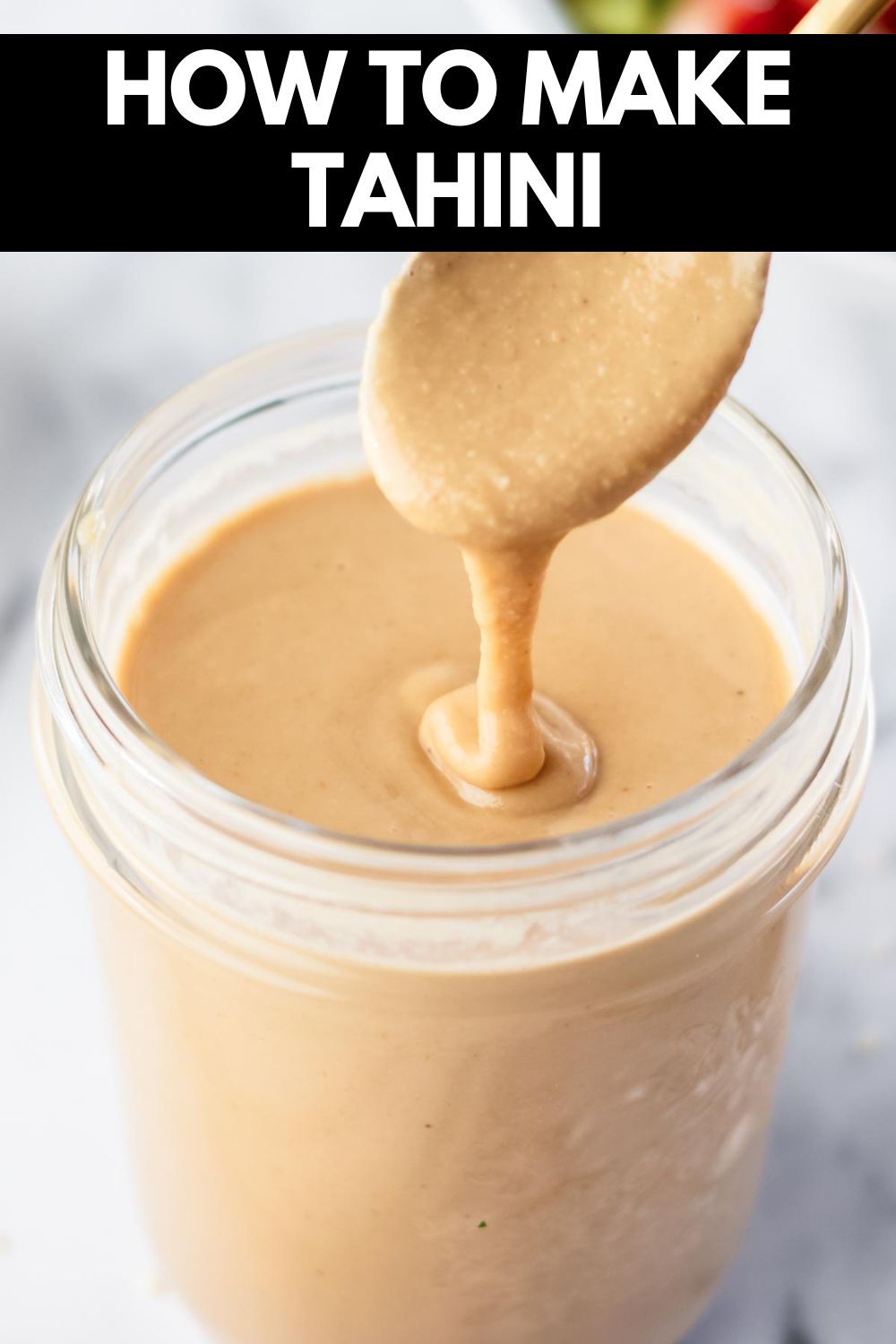 homemade tahini in a mason jar with a spoon drizzling it back in with homemade tahini in text for pinterest.