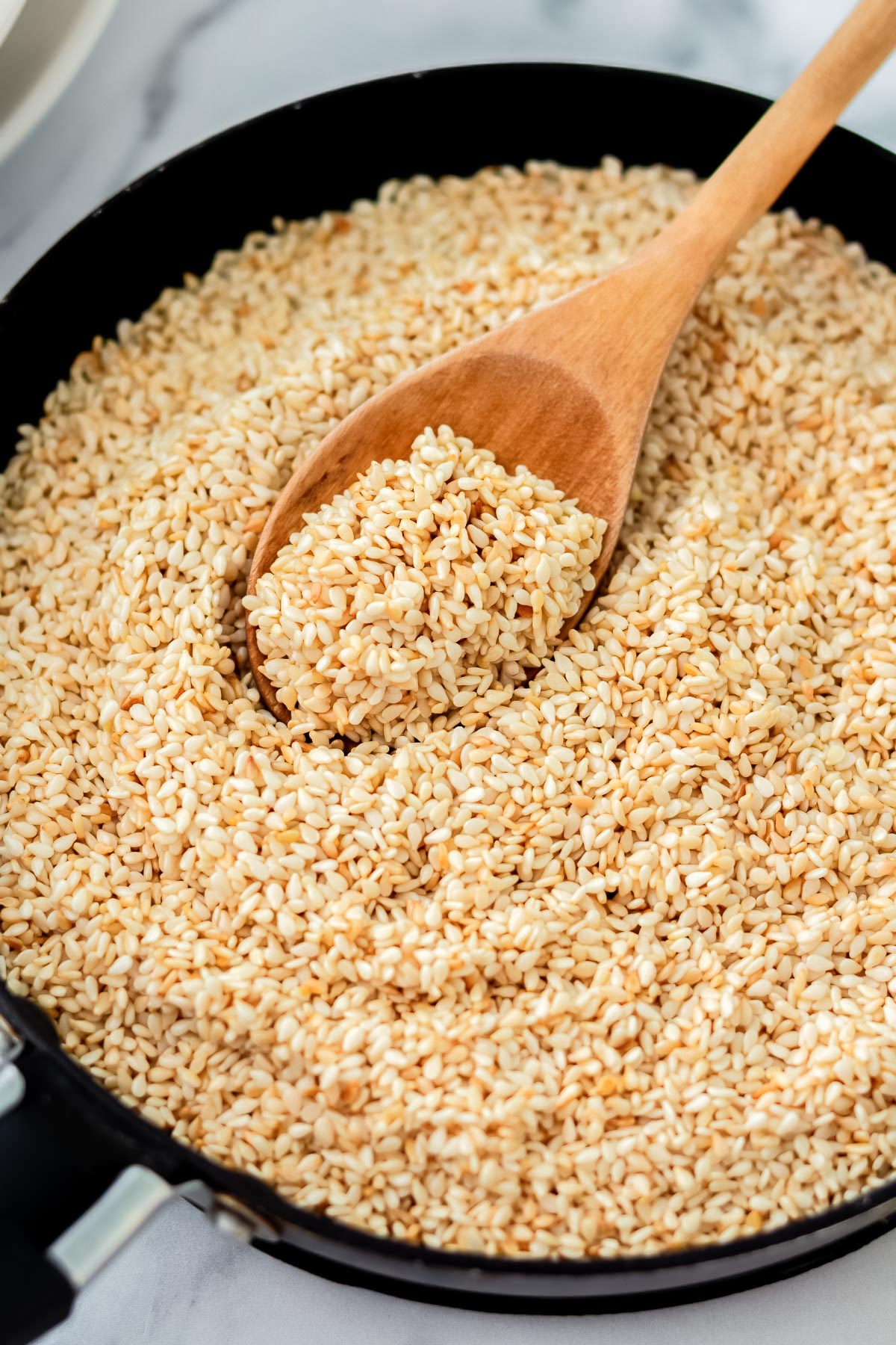 toasted sesame seeds in a pan and on the mixing spoon.