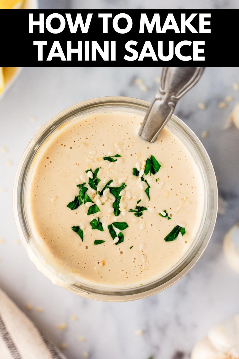 tahini sauce in a mason jar garnished with parsley and sesame seeds in it with a spoon inside it too.