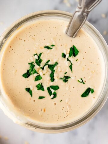 tahini sauce in a mason jar with a spoon in it and garnished with parsley and sesame seeds on top.