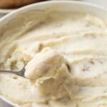 microwave mashed potatoes in a white low bolw with a spoon scooping some out.